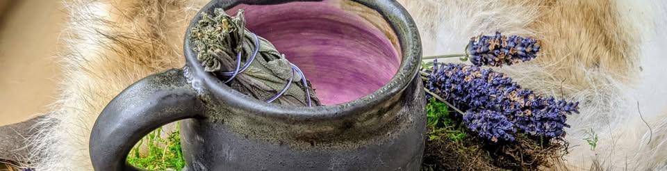A dark stoneware mug with a lavender interior, holding a sage bundle beside dried lavender