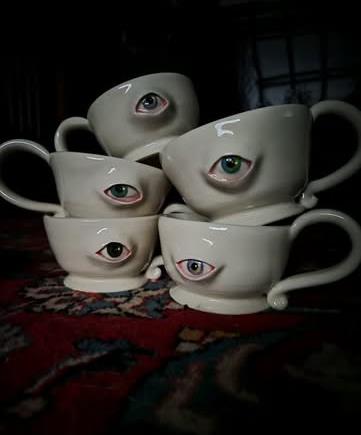A stack of white teacups, each with a sculpted eyeball